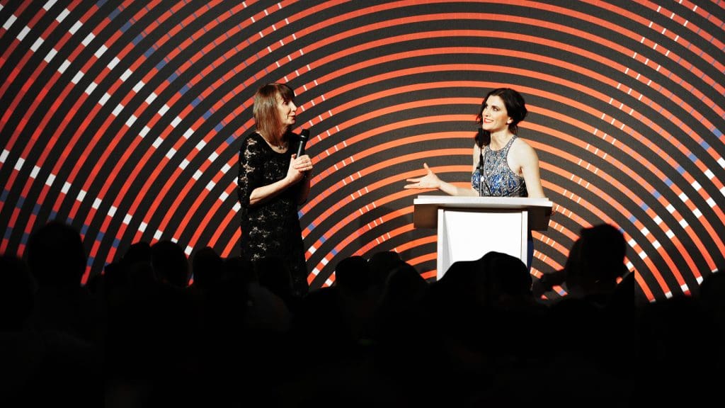 Two women are having a conversation on stage in front of a branded British Cycling Awards bright red backdrop. The host is Sky Sports News presenter and cycling broadcaster Orla Chennaoui, and she's talking to three-time Grand Tour runner up Philippa York.