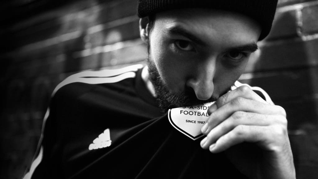 Black and white photograph of a model kissing the badge on his football shirt. The badge is the Powerleague logo.