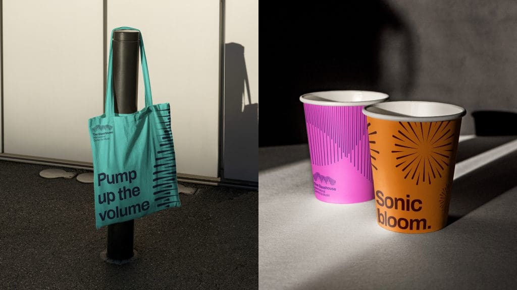 The image frame is split in half. The left side shows a bright blue tote bag hanging on a bollard, with the text on the bag reading 'Pump up the volume'. The image on the right is of two disposable coffee cups, one orange and one pink. The one in the foreground is orange and has a circular burst pattern with the text 'Sonic Bloom' applied. The one in the background is bright pink with a soundwave graphic. These images show the brand application on products at The Glasshouse.